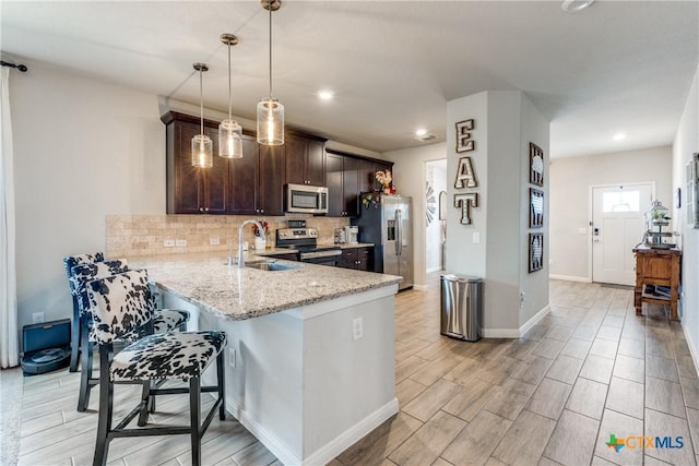 kitchen featuring tasteful backsplash, appliances with stainless steel finishes, a breakfast bar, dark brown cabinetry, and light stone countertops