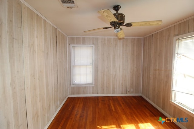 spare room featuring hardwood / wood-style flooring, ceiling fan, wood walls, and ornamental molding