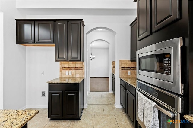 kitchen with light stone countertops, light tile patterned floors, decorative backsplash, appliances with stainless steel finishes, and arched walkways