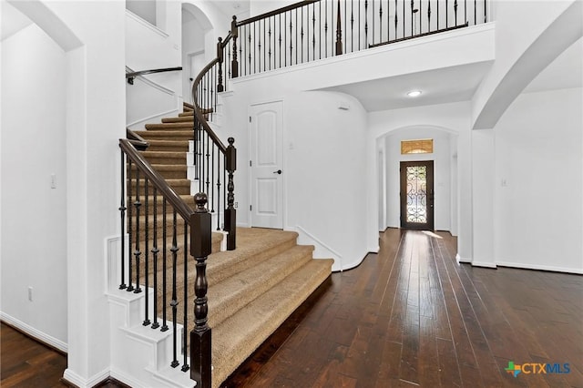 foyer entrance featuring baseboards, stairway, a high ceiling, arched walkways, and dark wood-style flooring