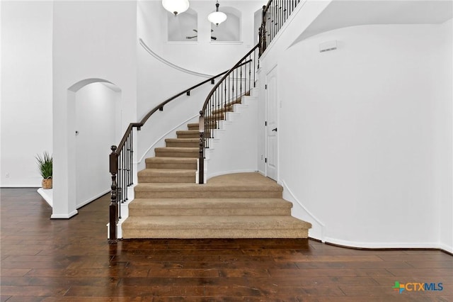 stairs with baseboards, arched walkways, a towering ceiling, and hardwood / wood-style flooring