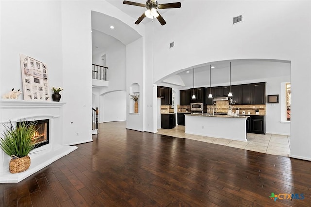 unfurnished living room with visible vents, light wood-type flooring, a high ceiling, a glass covered fireplace, and a ceiling fan