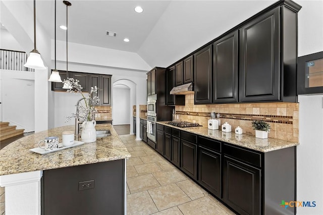 kitchen with a center island with sink, under cabinet range hood, decorative backsplash, light stone countertops, and stainless steel gas cooktop