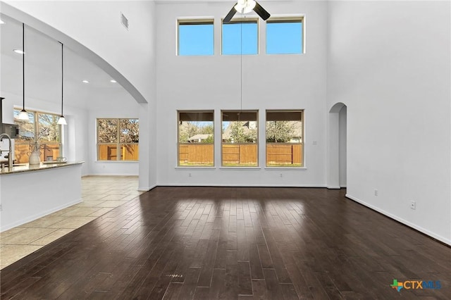 unfurnished living room featuring visible vents, wood finished floors, a ceiling fan, and arched walkways