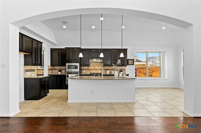 kitchen featuring light stone counters, visible vents, arched walkways, under cabinet range hood, and appliances with stainless steel finishes