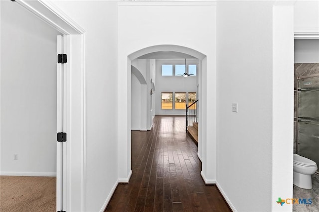 hallway featuring baseboards, arched walkways, dark wood-style floors, and stairs