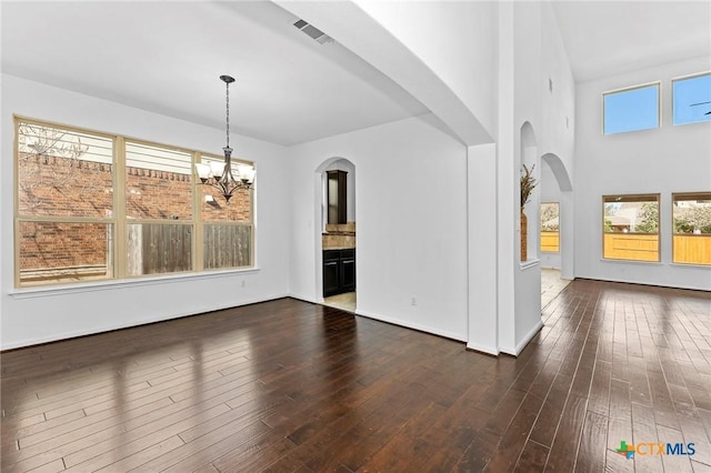 interior space featuring visible vents, baseboards, dark wood finished floors, an inviting chandelier, and arched walkways