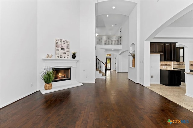 unfurnished living room with baseboards, a lit fireplace, light wood-style flooring, a high ceiling, and arched walkways