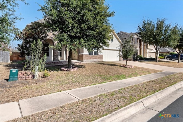 view of property hidden behind natural elements featuring an attached garage, fence, driveway, and stucco siding