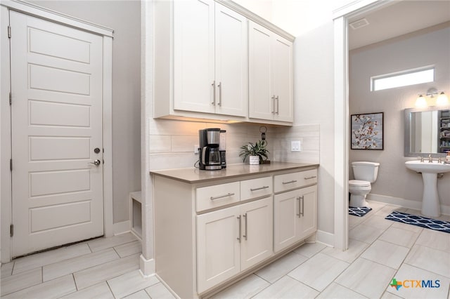 bar with decorative backsplash and white cabinetry