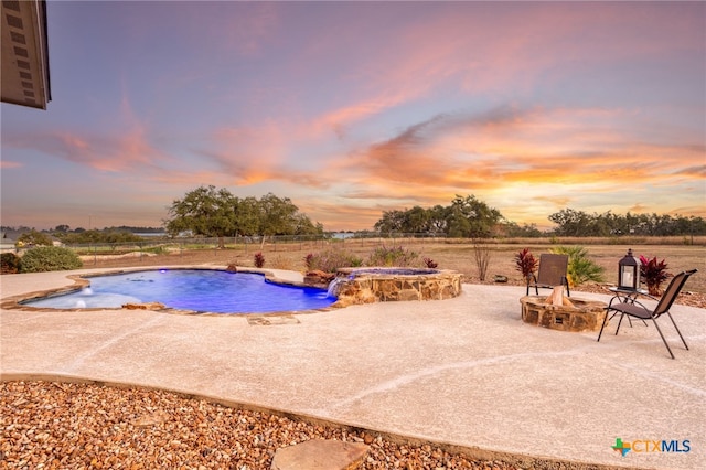 pool at dusk featuring pool water feature, an outdoor fire pit, and a patio