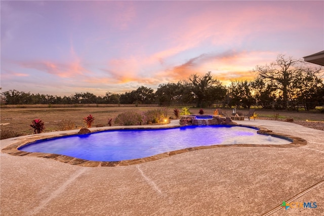 pool at dusk featuring pool water feature, an in ground hot tub, and a patio