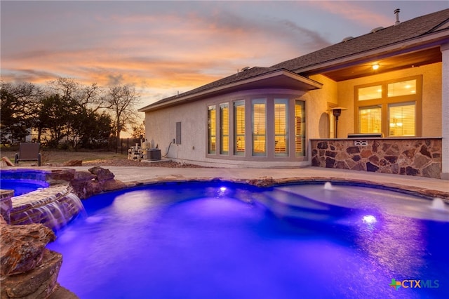 pool at dusk with an in ground hot tub, pool water feature, and a patio