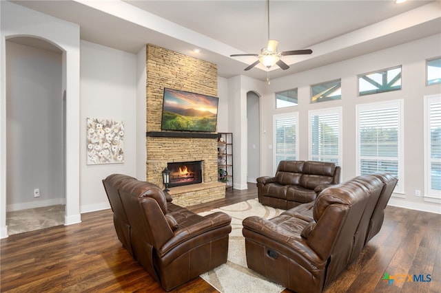 living room featuring ceiling fan, a stone fireplace, and dark wood-type flooring