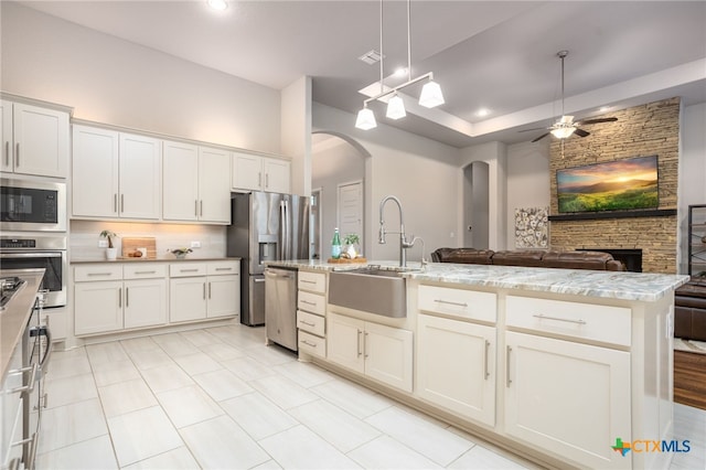 kitchen featuring stainless steel appliances, a kitchen island with sink, sink, decorative light fixtures, and white cabinets