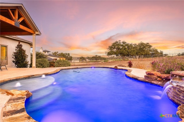 pool at dusk featuring pool water feature and a patio area