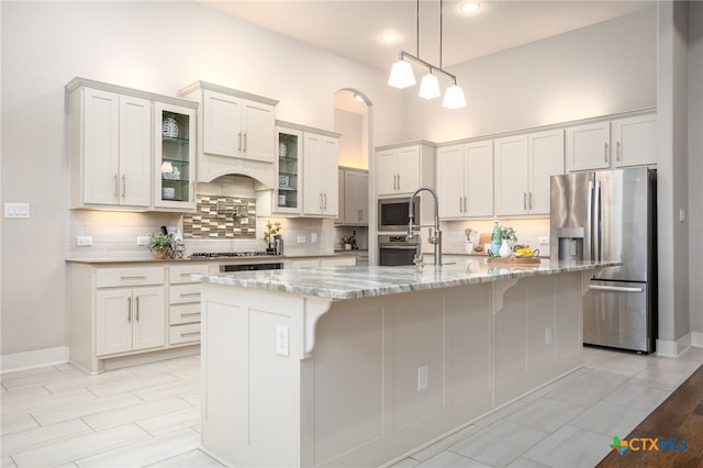 kitchen with white cabinetry, a kitchen island with sink, light stone counters, and appliances with stainless steel finishes