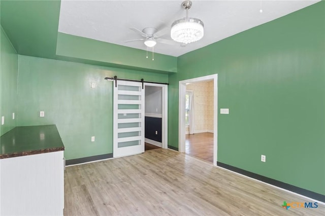 1200 4th St, Palacios, TX 77465 - spare room with a barn door, ceiling fan, wood finished floors, baseboards, and a chandelier