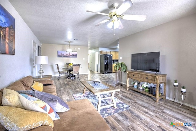 living room with a textured ceiling, ceiling fan, and light hardwood / wood-style flooring