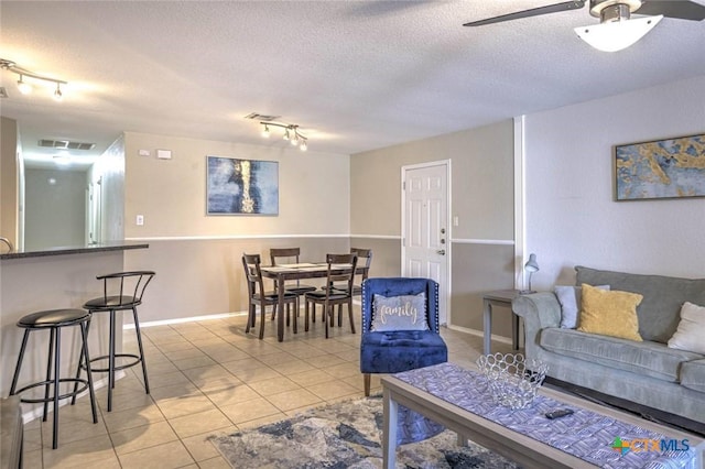 tiled living room featuring rail lighting, a textured ceiling, and ceiling fan