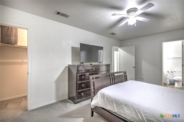 bedroom featuring ensuite bath, a textured ceiling, a walk in closet, ceiling fan, and light carpet