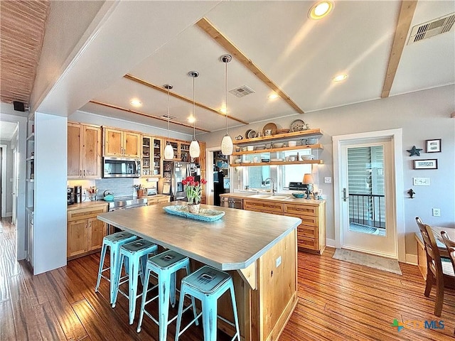 kitchen featuring hardwood / wood-style floors, beam ceiling, appliances with stainless steel finishes, and a kitchen island