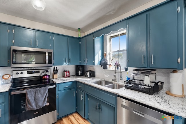 kitchen featuring blue cabinetry, sink, backsplash, light hardwood / wood-style floors, and appliances with stainless steel finishes