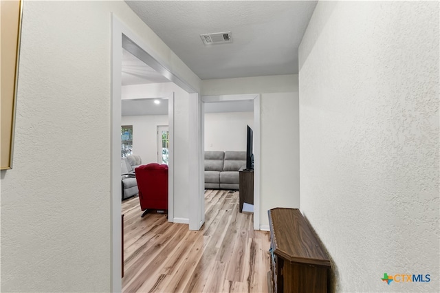 corridor with light hardwood / wood-style floors and a textured ceiling