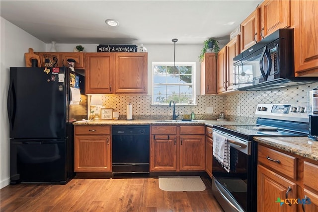 kitchen with black appliances, wood finished floors, brown cabinetry, and a sink