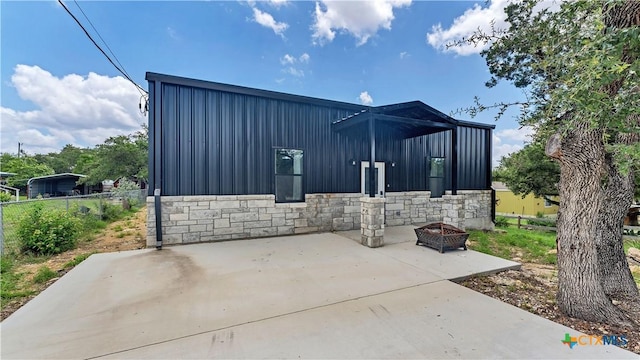 view of side of property with board and batten siding, a patio area, stone siding, and an outdoor fire pit