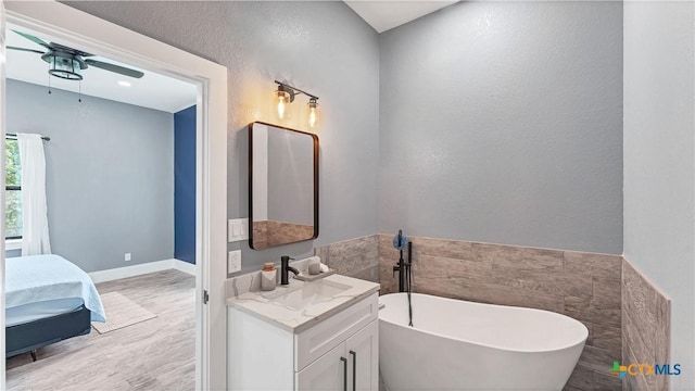 ensuite bathroom with connected bathroom, vanity, a ceiling fan, a freestanding tub, and wood finished floors