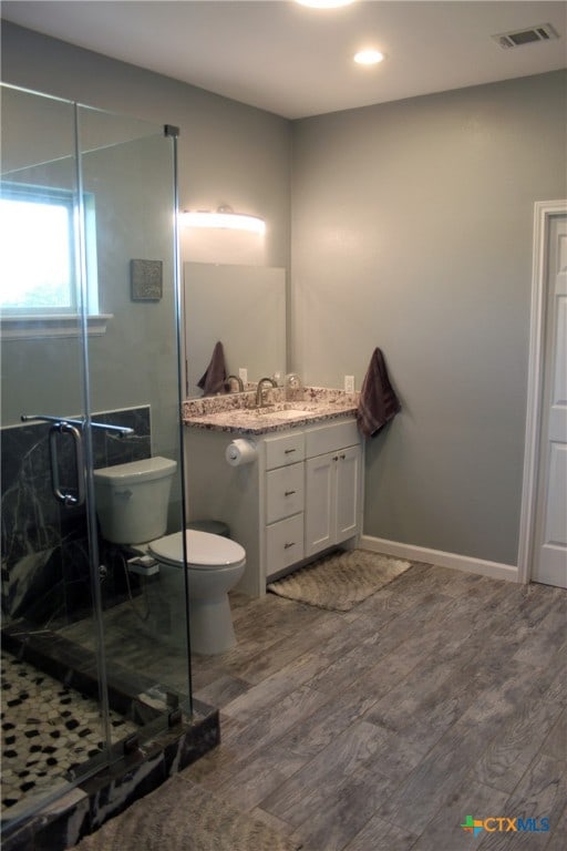 bathroom featuring hardwood / wood-style floors, walk in shower, vanity, and toilet