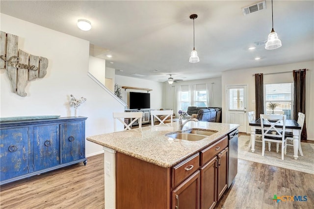 kitchen featuring sink, decorative light fixtures, stainless steel dishwasher, a kitchen island with sink, and light hardwood / wood-style floors