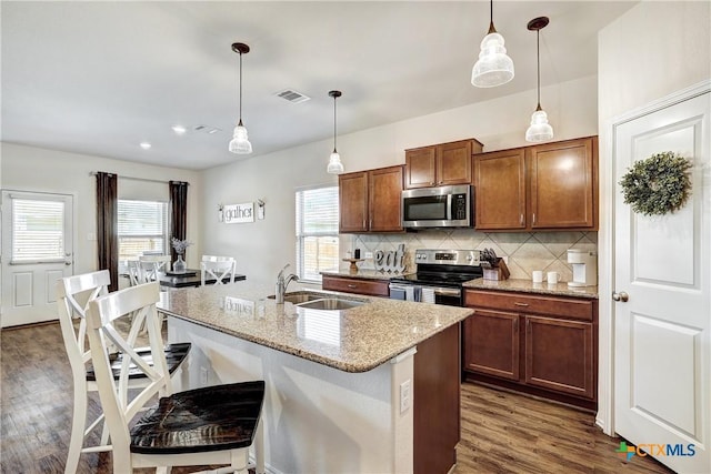 kitchen with stainless steel appliances, a kitchen island with sink, sink, and hanging light fixtures