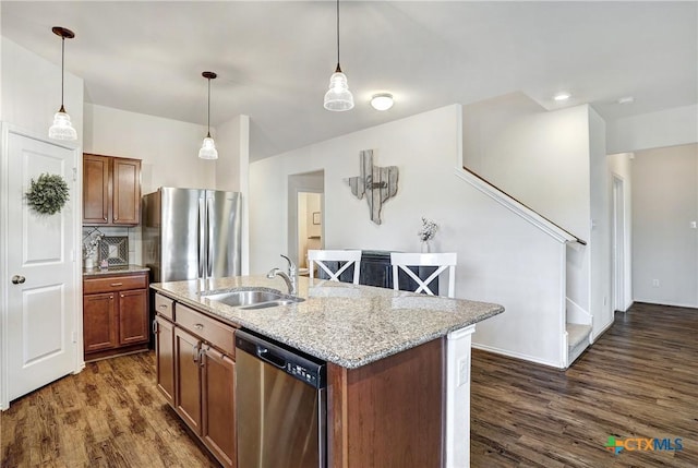 kitchen featuring sink, appliances with stainless steel finishes, an island with sink, decorative backsplash, and decorative light fixtures