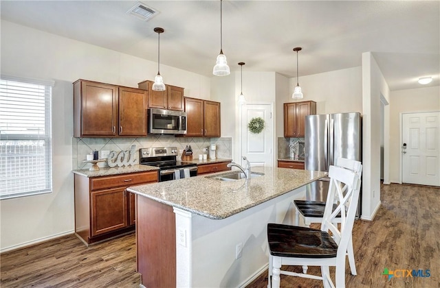 kitchen featuring sink, a breakfast bar area, appliances with stainless steel finishes, a kitchen island with sink, and decorative light fixtures