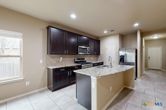 kitchen featuring light stone counters, stainless steel appliances, visible vents, decorative backsplash, and a sink