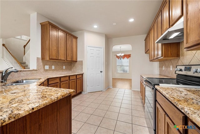 125 Big Timber Dr, Temple, TX 76502 - kitchen with stainless steel range with electric cooktop, under cabinet range hood, brown cabinets, arched walkways, and backsplash