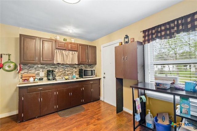 kitchen featuring a sink, stainless steel microwave, wood finished floors, light countertops, and decorative backsplash