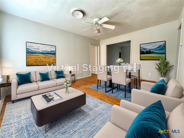 living room featuring ceiling fan, a textured ceiling, baseboards, and wood finished floors