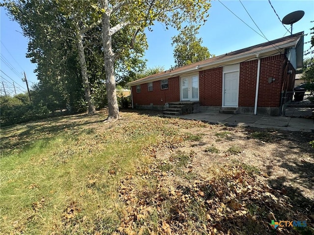 exterior space featuring entry steps, french doors, brick siding, and a front yard