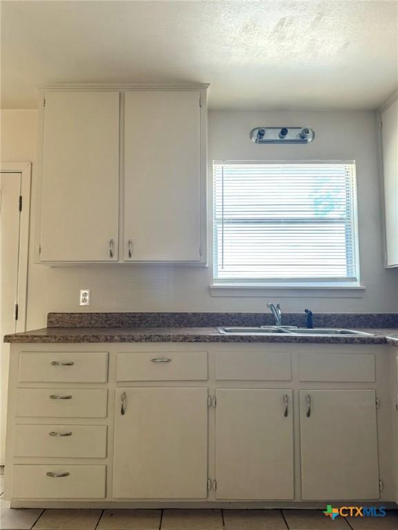 kitchen featuring light tile patterned floors, a textured ceiling, a sink, white cabinets, and dark countertops