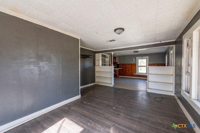 unfurnished living room featuring wooden walls, crown molding, and dark wood-type flooring