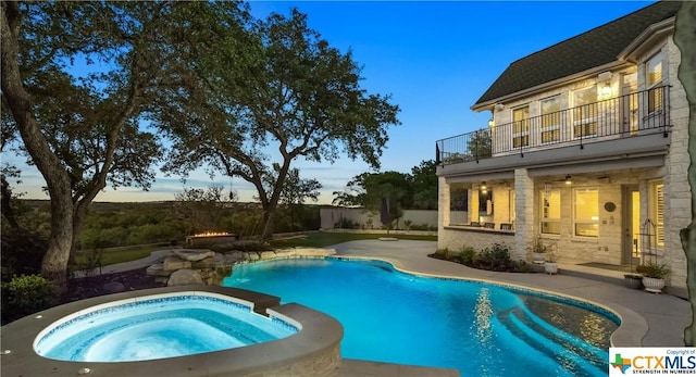 pool at dusk featuring a patio area and an in ground hot tub