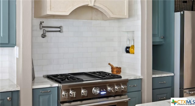 kitchen with backsplash, light stone counters, blue cabinets, and appliances with stainless steel finishes