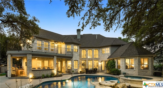 back house at dusk with a swimming pool with hot tub, a balcony, and a patio area