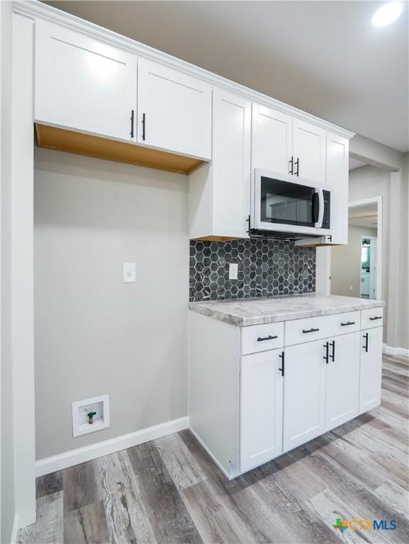 kitchen featuring decorative backsplash, white cabinets, light stone counters, and light wood-type flooring