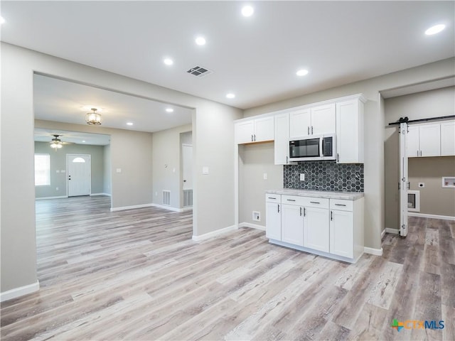 kitchen featuring backsplash, ceiling fan, a barn door, light hardwood / wood-style flooring, and white cabinets