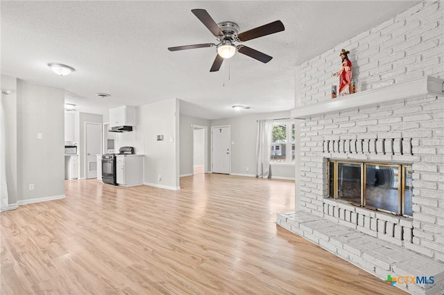 unfurnished living room with light wood-type flooring, a brick fireplace, baseboards, and a textured ceiling