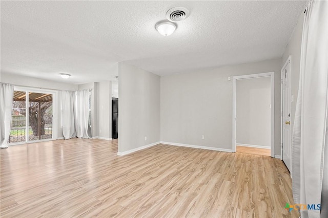 unfurnished room featuring light wood-style floors, visible vents, a textured ceiling, and baseboards